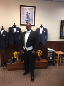 Man in tuxedo, surrounded by suits.