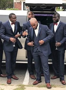 Groomsmen in suits by limousine.