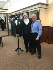 Groom and father in tuxedo shop.