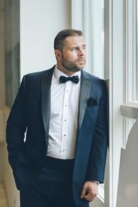 Man in tuxedo looking out window.