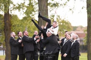 Groom lifted by his groomsmen outdoors.