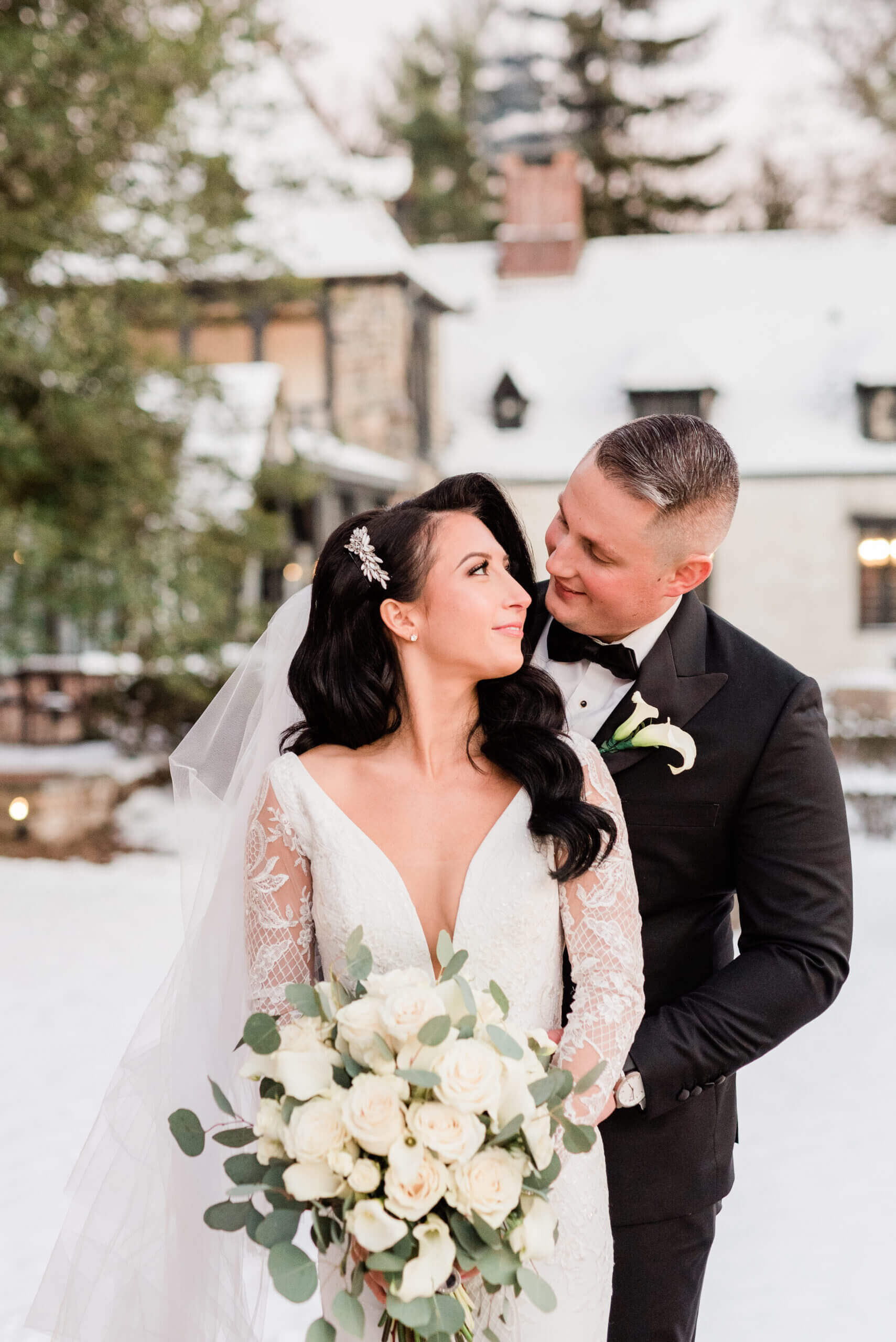 Bride and groom posing together outdoors in the snow, with the groom wearing a black tuxedo.