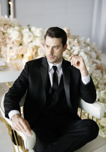 Man in black tuxedo sits thoughtfully.